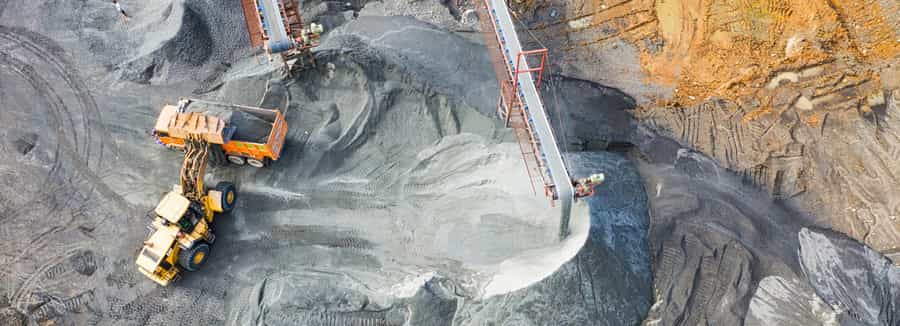 “Aerial view of a gold mining site with heavy machinery, including an excavator loading rocks into a truck and a conveyor system, illustrating the process of gold extraction.
